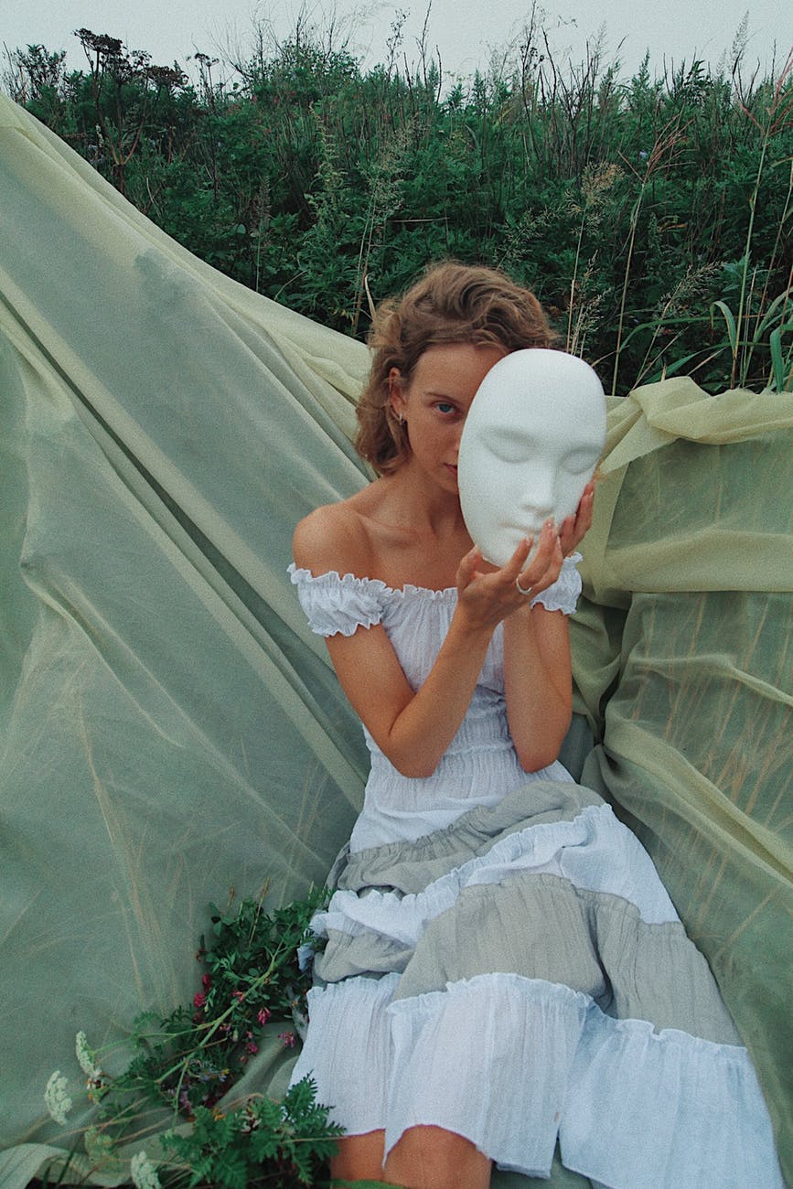 sitting woman wearing gray off shoulder dress holding mask