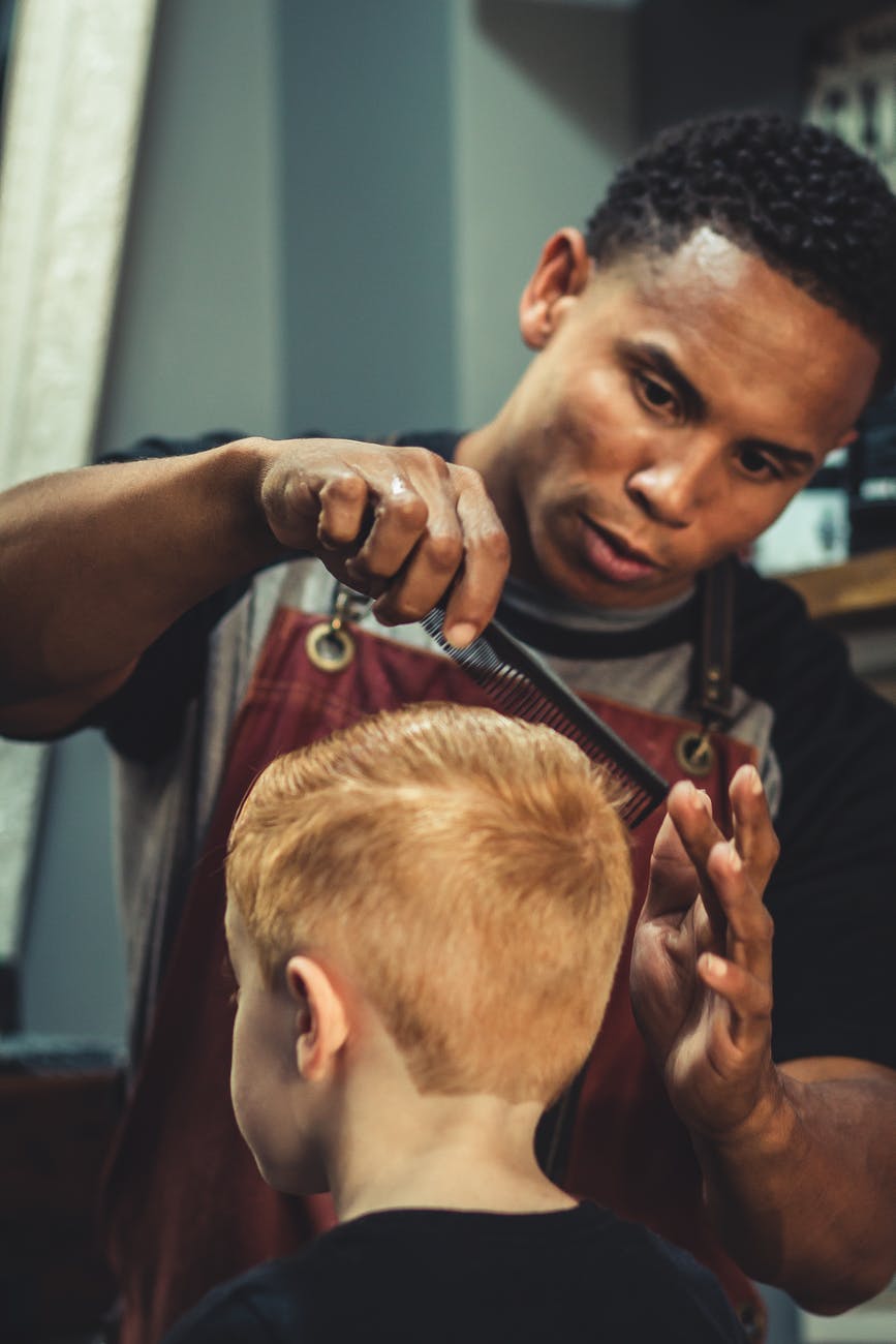 boy sitting trimmed by man holding scissor