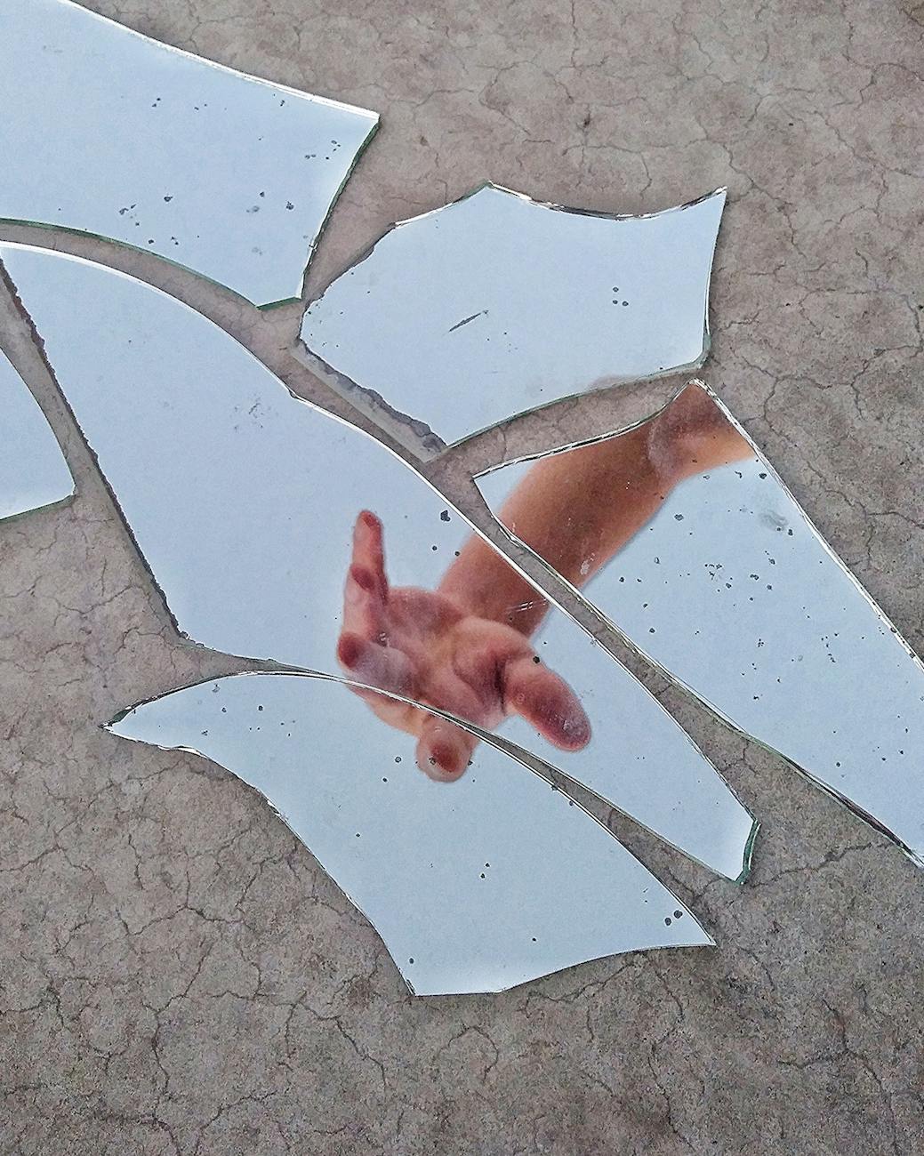 mirror fragments on gray surface with the reflection of a person s hand